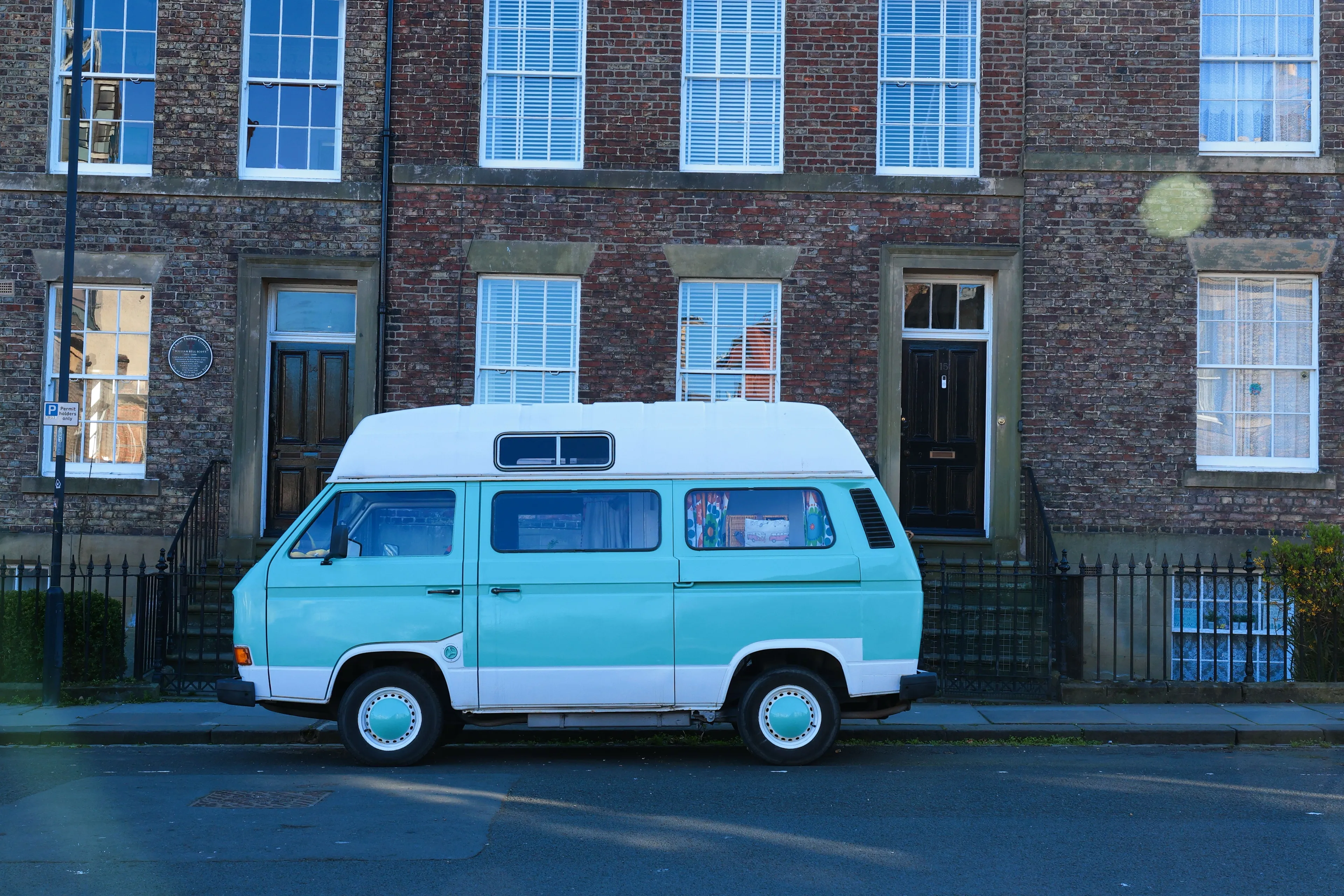 A red-brick Georgian terrace on a Newcastle street, with a turquoise camper van parked outside